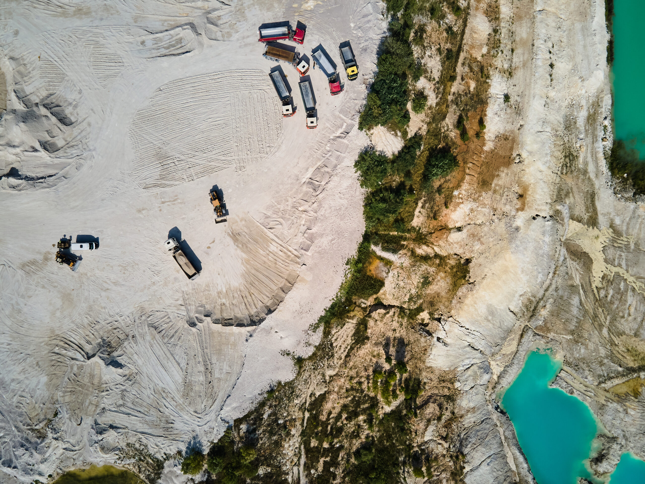 Aerial view trucks near quarry extraction porcelain clay, kaolin, with turquoise water and white shore, drone view open pit mine kaolin flooded with water