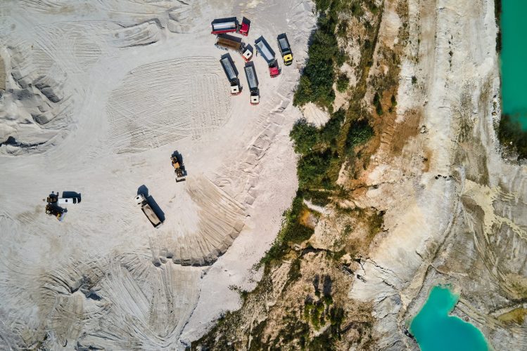 Aerial view trucks near quarry extraction porcelain clay, kaolin, with turquoise water and white shore, drone view open pit mine kaolin flooded with water